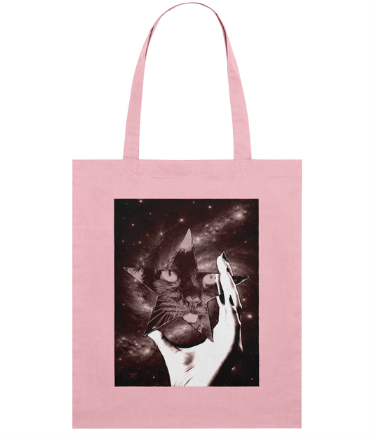 Pink tote bag with surreal art design printed on the front. The artwork features a woman's hand holding a star-shaped mirror in space, with a cat's face reflected in it.